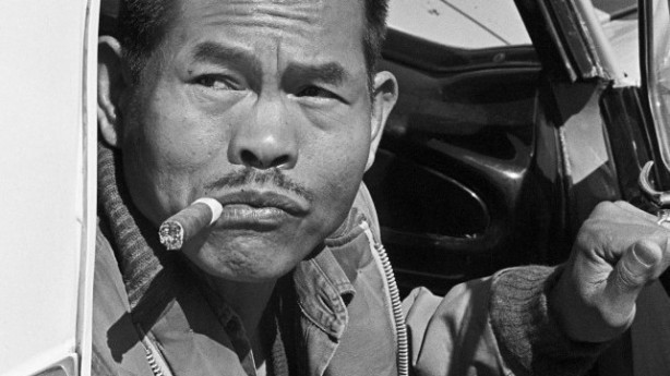 Black and white film still of man with cigar in his mouth looking off camera.