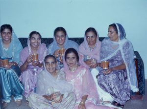 A group of women wearing traditional Punjabi outfits sit together on a couch to pose for the picture.