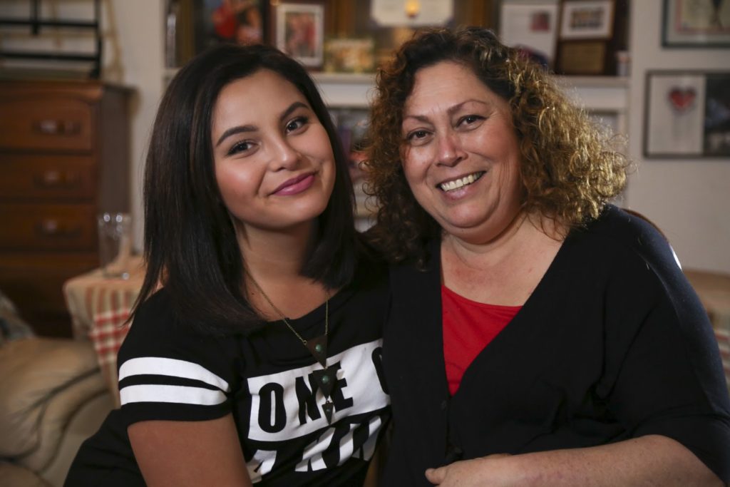 A young woman and her mother sit together, smiling at the camera.