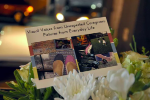 A card sits in a bouquet of flowers. There is a photocollage on the card, and the words "Visual Voices from Unexpected Caregivers: Pictures from Everyday Life."