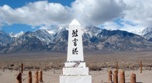 A vast empty landscape with a range of snow-capped mountains in the distance. In the foreground is a memorial obelisk engraved with Japanese writing. 