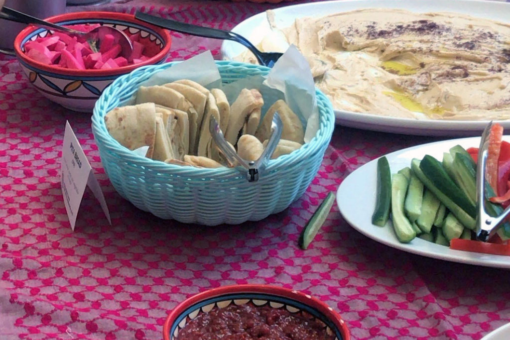 Baskets and platters of food on a colorful tablecloth from Reem's Catering.