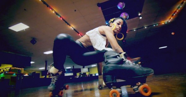 A young African American woman wearing black roller skates performing a skate trick.