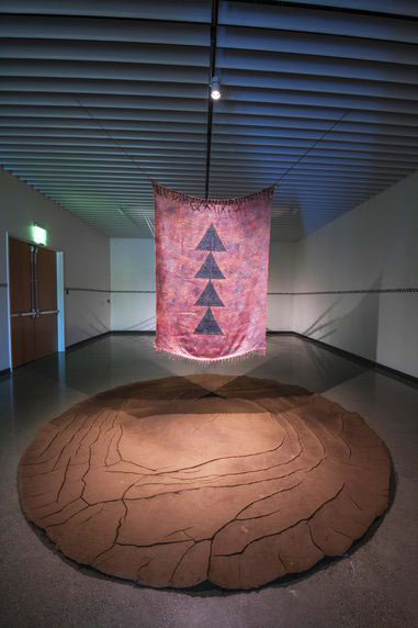 A reddish fabric with symbols hangs over a round mud-like object.