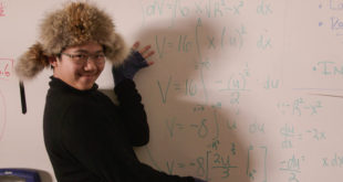 A teenage student sits next to a whiteboard with math equations on it.