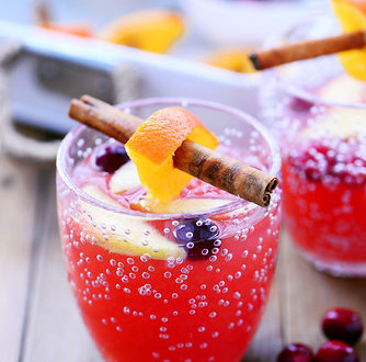A photo of a glass filled with cranberry orange holiday punch topped with a cinnamon stick.