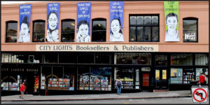 The front of the City Lights Booksellers and Publishers store showing tons of books inside the windows and blue banners with drawings of people.