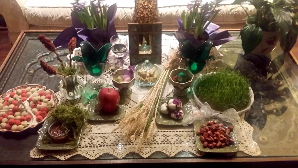 A photo of a table set with flowers, plants, fruit, nuts, and other items to celebrate the Nowruz New Year. 