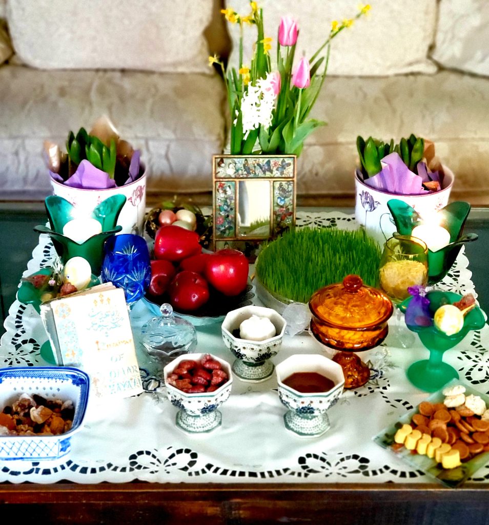 A photo of a table set with flowers, plants, fruit, nuts, and other items to celebrate the Nowruz New Year. 