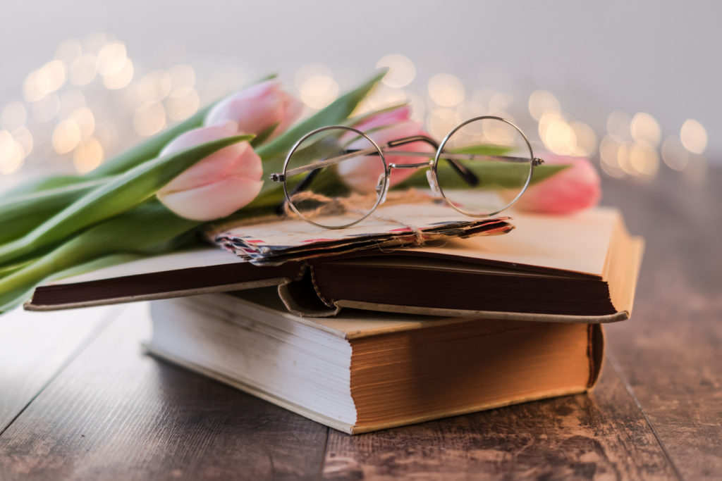 A stack of books with a few pink tulips and a pair of eyeglasses on top.