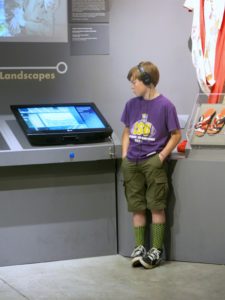 A young person stands with headphones looking at an exhibit screen.