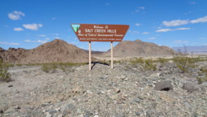 A brown sign with text in the center of rocks and mountains.