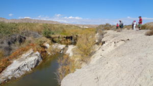 A group of people look at the creek and waterfall between the rocks.
