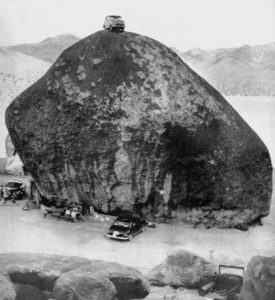 Black and white photo of Giant Rock with a car on top.