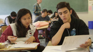 Two students sit at their desks in discussion inside a classroom.