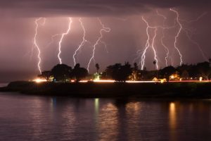 Multiple flashes of lightning over a city next to water.