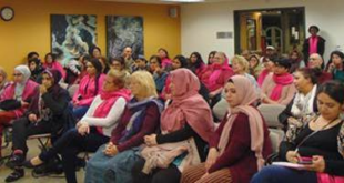 A large group of people sit in the library. Many of them wear colorful head scarves.