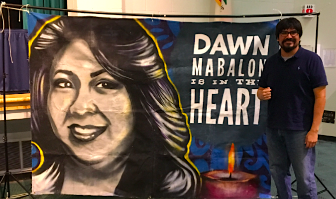 Oliver stands next to a banner with a photo of Dawn Mabalon.