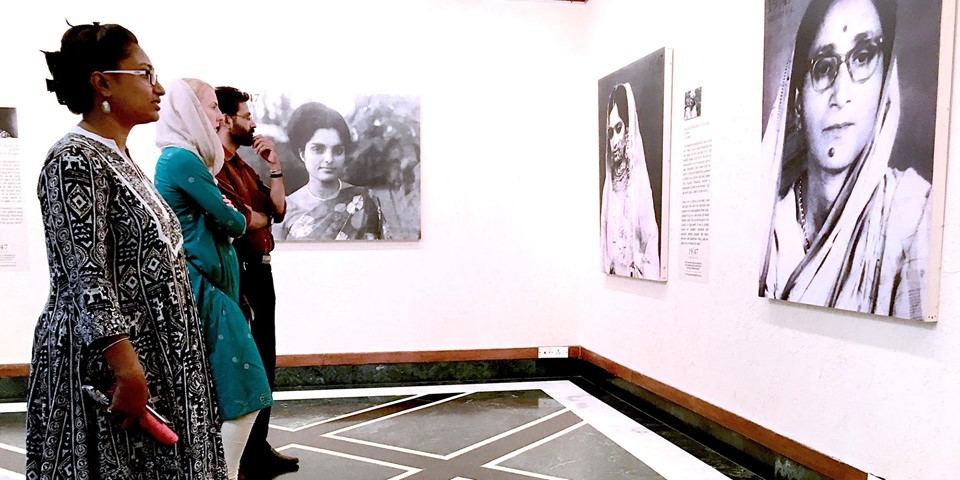 A group of persons standing in a gallery looking at portraits on the wall.