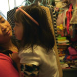 An adult and child stand close together in a clothing store.