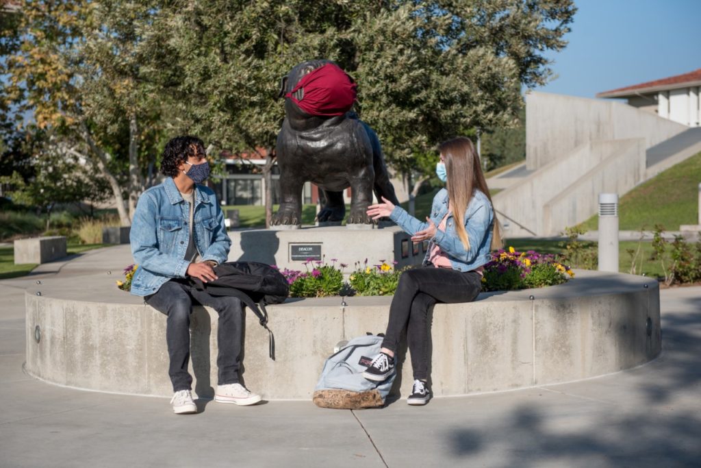 Students sit outside near a statue talking,