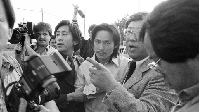 A black and white photo of a group of reporters are surrounding a man.