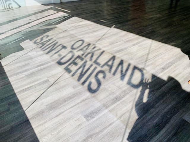 Various shadows flow cross a floor spelling out Oakland Saint-Denis.