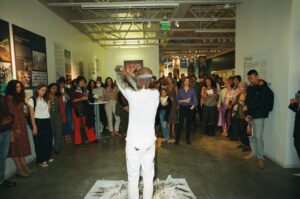 A visual performance artist stands in front of a crowd in an art gallery.