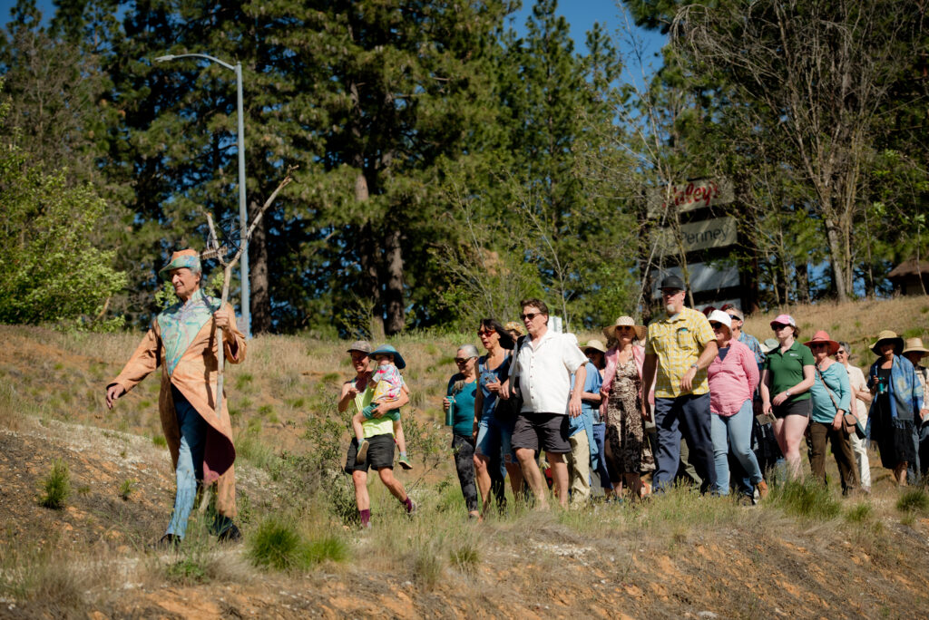 Cast member of Project Wild Edges holding a "Y" shaped branch and leading a group of attendees along a trail.