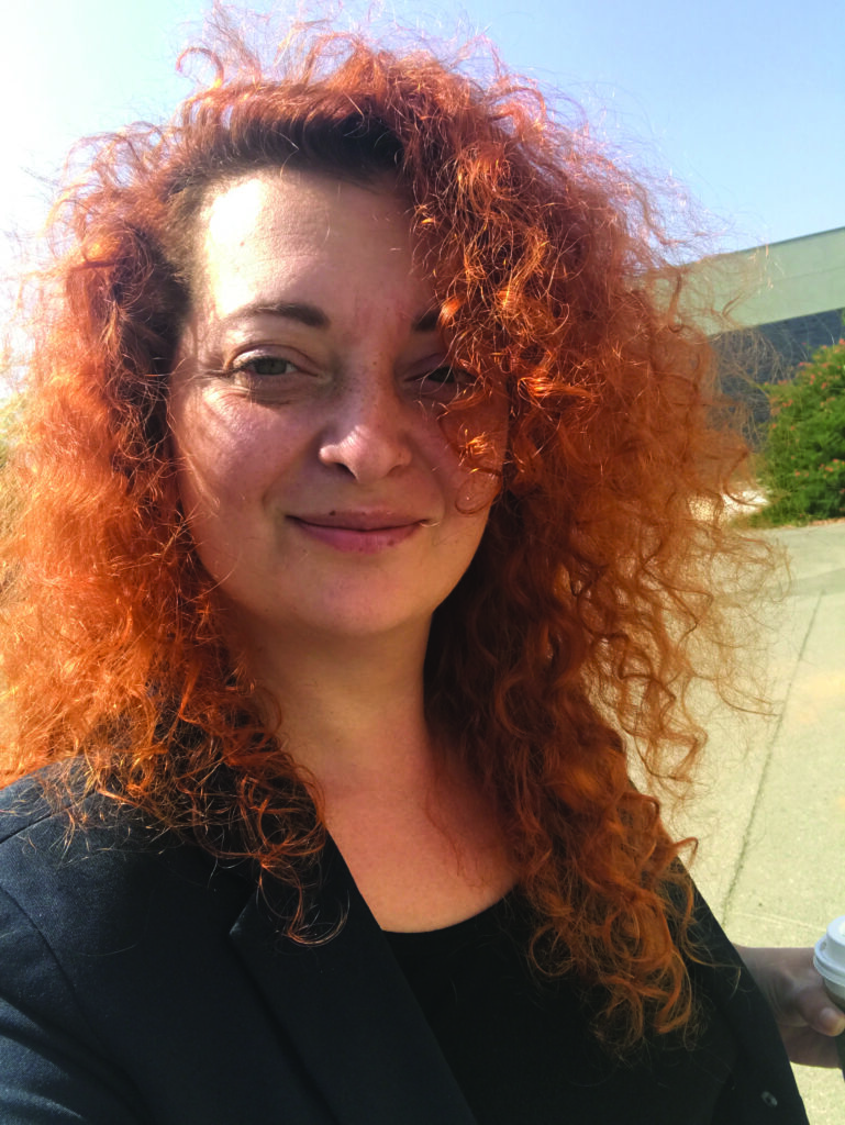Photo portrait of a woman with curly red hair and black top.