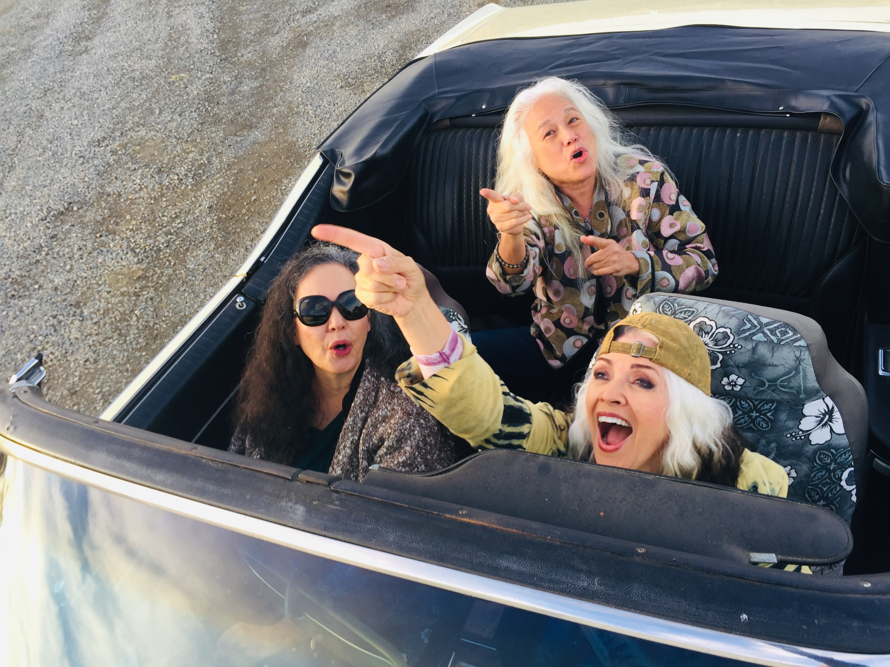 Three women smiling in a convertible car.