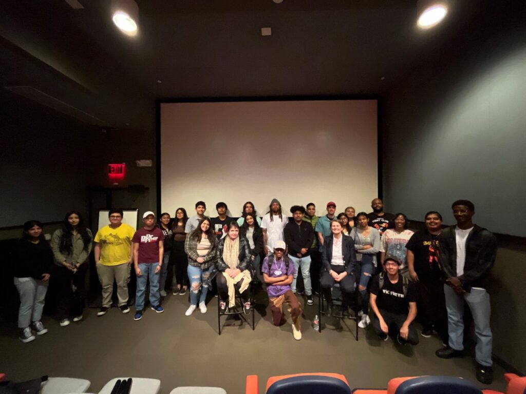 Group of people pose in front of a movie screen inside a screening room.