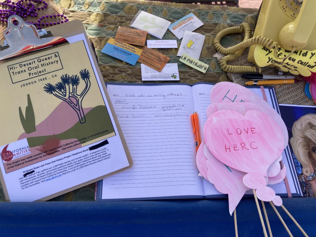 Close-up of items on a table, include a clipboard with project art and California Humanities logo, a sign up sheet, and yellow telephone.