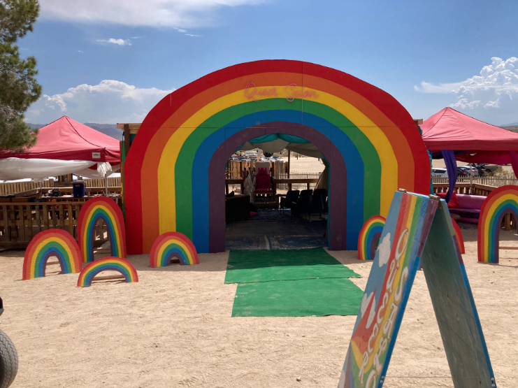 Looking towards the entryway of a tent that has a rainbow entrance and words Queer Salon affixed above the entryway