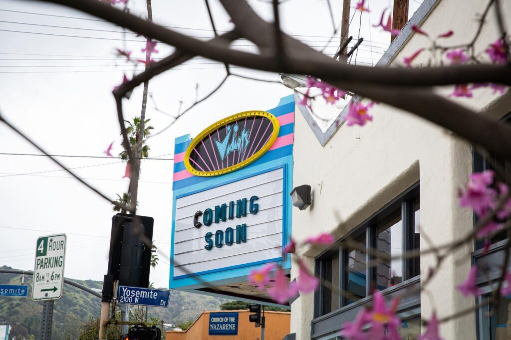 Exterior of theater showing marquee in light blue with words "Coming Soon" and Vidiots logo