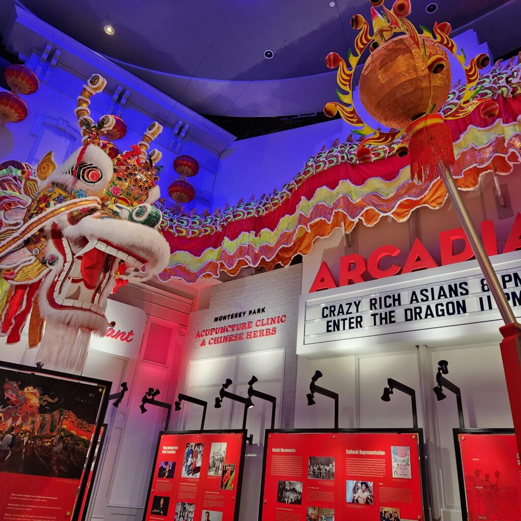 Part of a museum exhibit, showing a large dragon and replica of theater marquee reading ARCADIA and films listed (Crazy Rich Asians and Enter the Dragon)