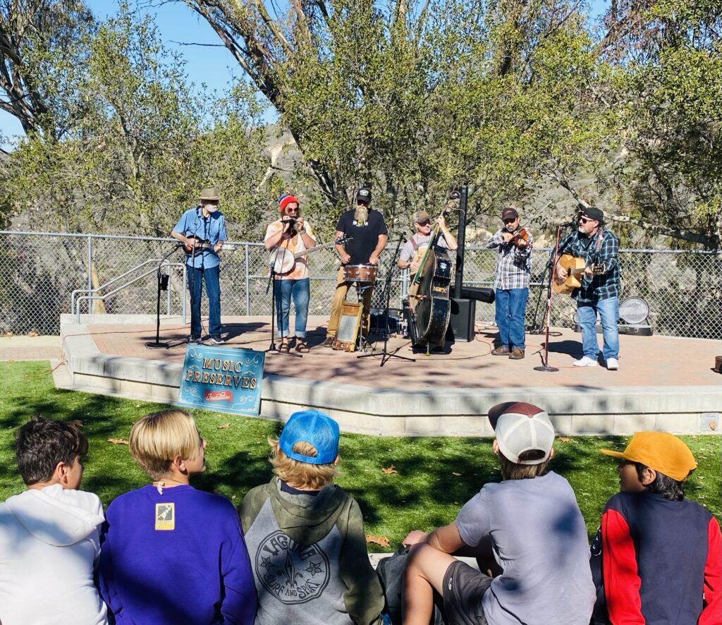 A group of musicians perform with bluegrass instruments on stage outside.