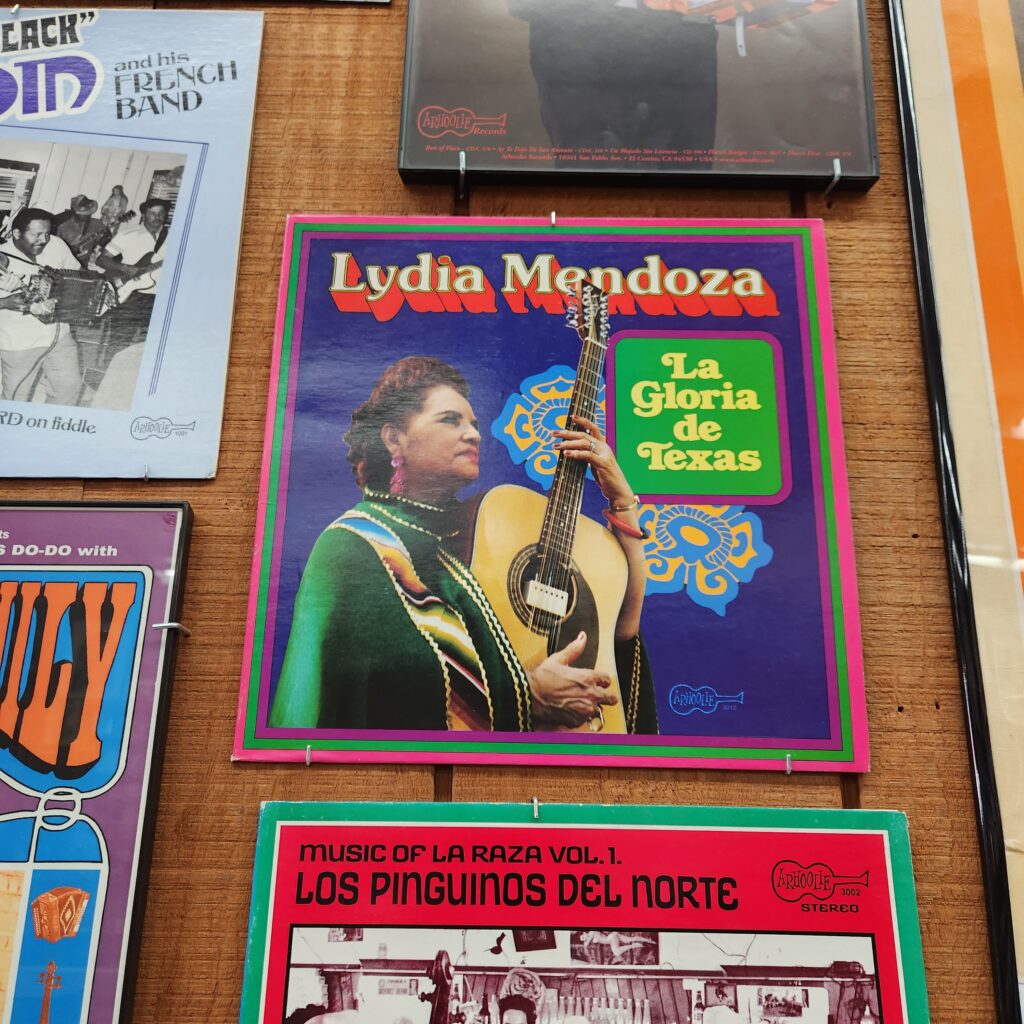 Colorful record cover mounted on a wall showing a woman carrying a guitar with title Lydia Mendoza La Gloria de Texas