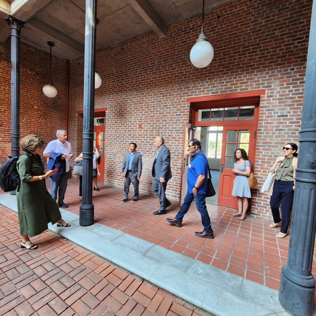 People stand inside a courtyard with brick floor, white bulb lamps hanging from the second floor