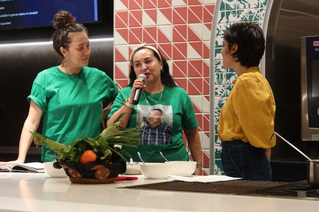 Three women during a program. Two women wear green tshirts, the other wears a yellow shirt.