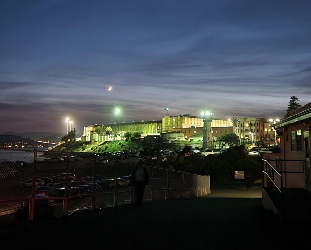 Night shot of exterior of prison buildings, lit up by floodlights.