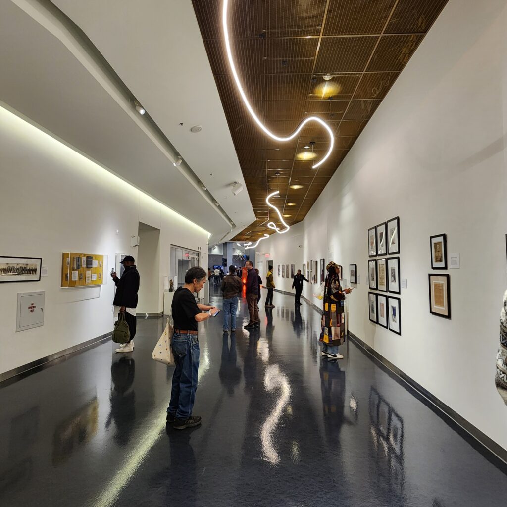 Looking down the corridor of an art gallery, with wavy light fixtures on the ceiling