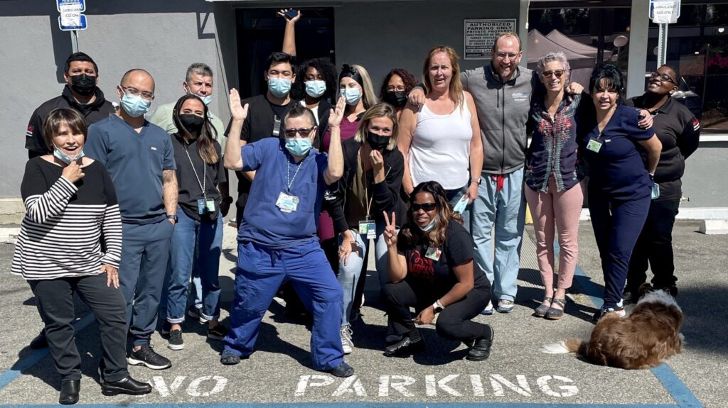 A group of medical staff and patients pose boisterously in a parking lot.
