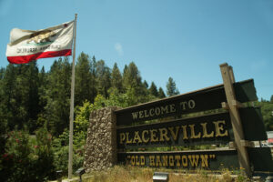 Wooden sign reading "Welcome to Placerville" with Califoria bear flag flying on a pole beside it.