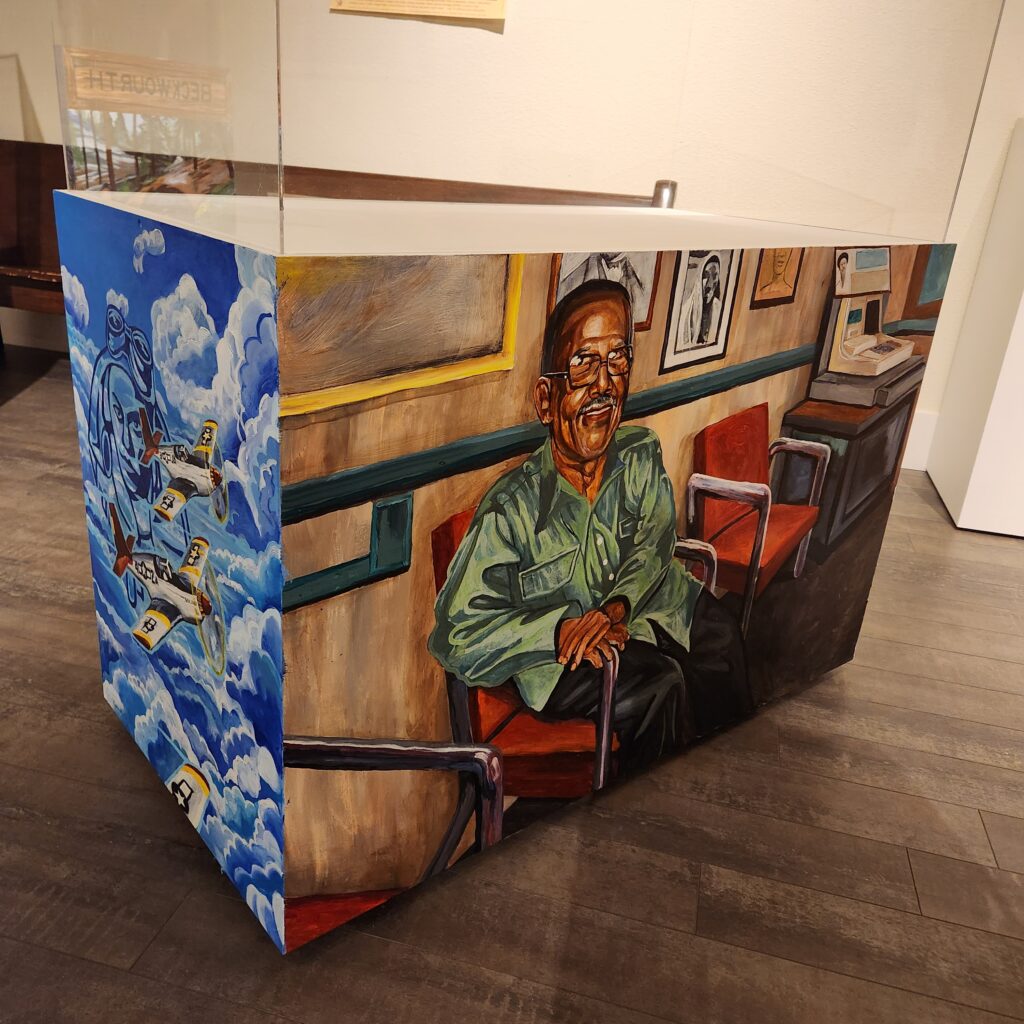 Mural on a museum pedestal of a man wearing a green shirt sitting in front of wood paneled wall