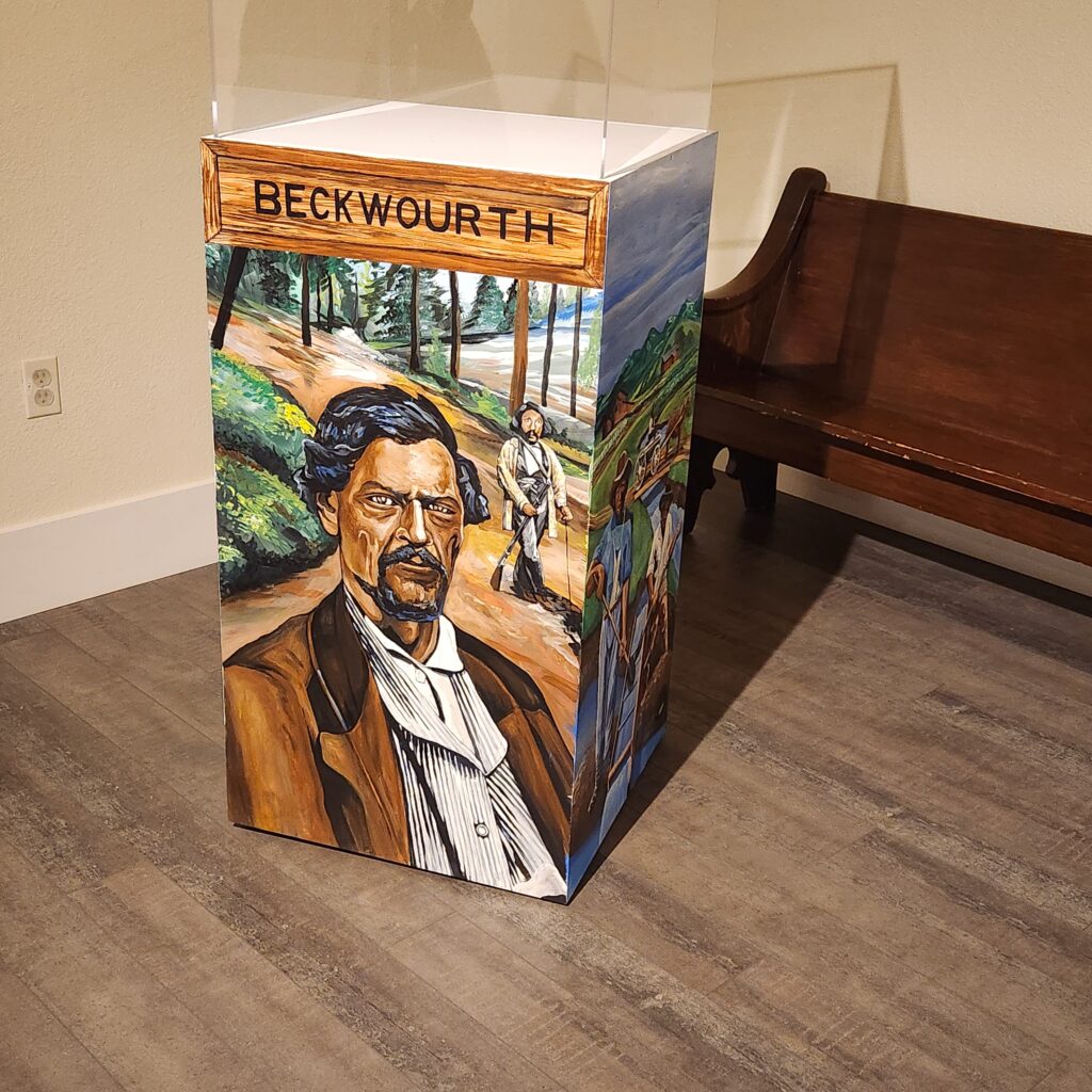 Mural on a museum pedestal of a man in a formal brown coat, forest scene behind him. Text reads "Beckwourth"